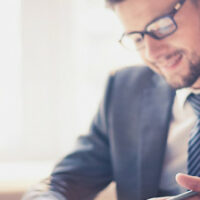 Image of two young businessmen using touchpad at meeting