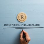 Letter R cut into wooden cut circle and male hand writing a Registered trademark sign under it
