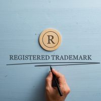 Letter R cut into wooden cut circle and male hand writing a Registered trademark sign under it